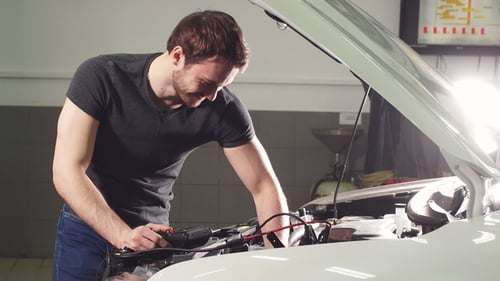 Young Technician Man Making Engine Service of Car in Garage.