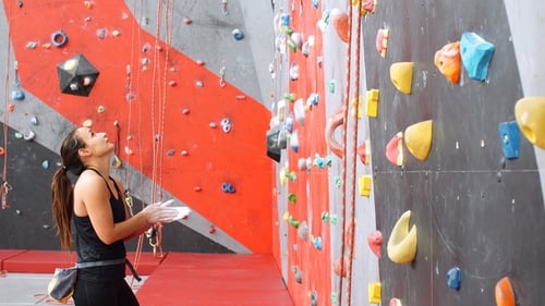 Belle jeune femme commence à grimper sur un grand mur artificiel.