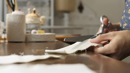 Woman Cuts White Fabric with Scissors Indoors