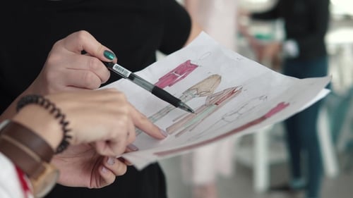 Young Fashion Designer, Tailor and Dressmaker Works with an Assistant and Looks at the Sketch of