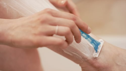 Perna de barbear de mão feminina no banheiro
