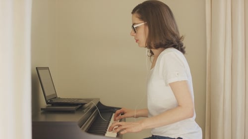 Woman Plays Piano at Home Next to Laptop