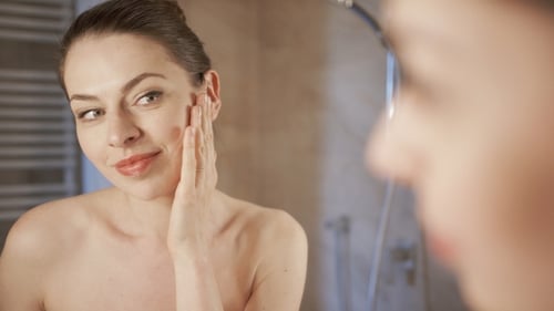 Woman Applies Lotion To Her Face In Bathroom