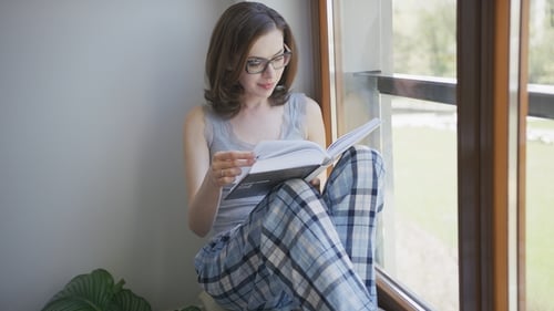 Woman Reads Book by Window at Home