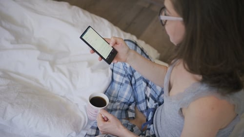 Woman Using Mobile Phone in Bed with Coffee