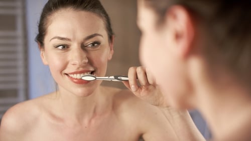 Woman Brushing Teeth in Bathroom Mirror