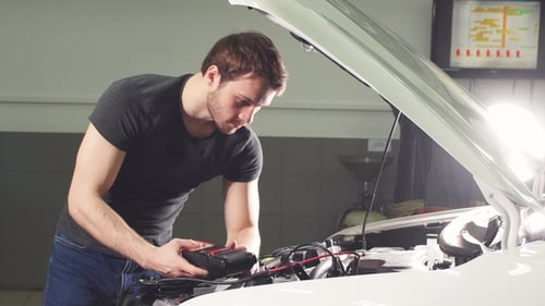 Car Mechanic Is Standing in an Auto Repair Shop Near Automobile with Open Hood and Making Notes.