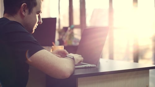 Young Business Man Wearing Glasses with a Clock on His Hands, Sitting at a Table, Doing Work on the