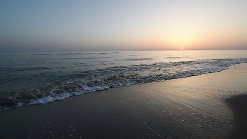 Ruhige Meereswellen am Sandstrand bei Sonnenuntergang. Sonnenreflexion im Meerwasser. Hintergrund aus der Natur