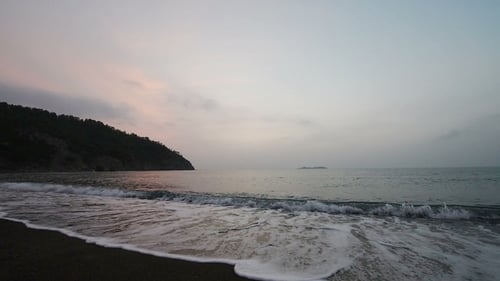 Calm Waves of the Sea on the Sandy Beach at Sunset. Sun Reflection in Sea Water. Nature Background