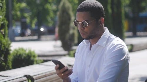 Afroamerikanischer Mann SMS-Texte mit App auf dem Smartphone in der Stadt.