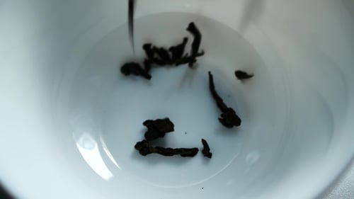 Tea Leaves Falling Into a White Bowl