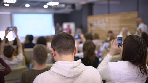 Diverse Crowd Attending Presentation Taking Pictures with Phones