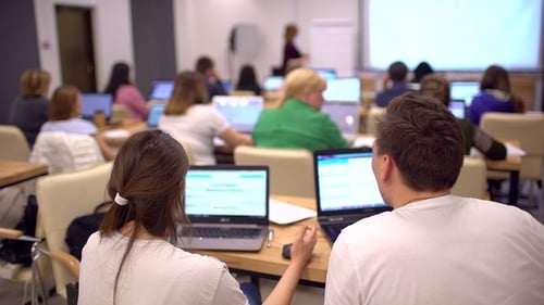 Group of Female and Male Students Are Sitting in a College Classroom and Looking at a Laptop