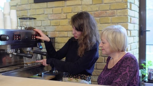 Young Woman Trains Adult Female On Espresso Machine