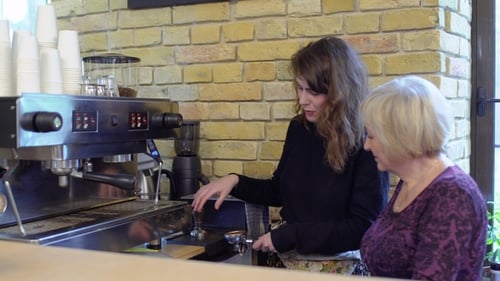 Young Woman Teaching Coffee Preparation to Adult at Cafe