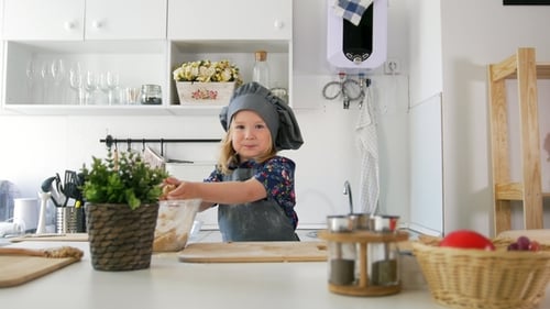 Cheerful Little Girl in Apron Rolls Out the Dough in the Kitchen