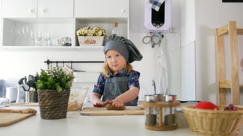 Little Caucasian Girl in Apron Rolls Out the Dough on the Board