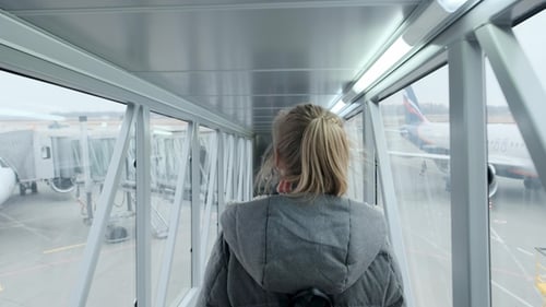 Woman Walks Through Jetway Towards Passenger Airplane