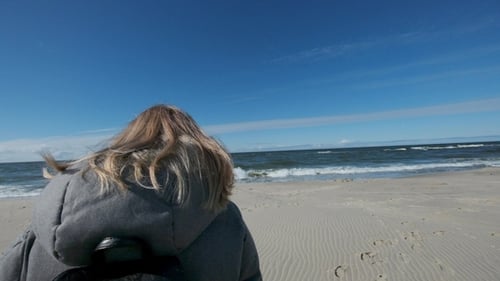Lovely Blonde Girl Steps on a Sandy Beach on a Background of Blue Sea Waves