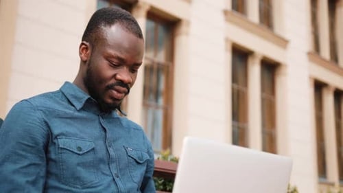 African American Bussinesman Sits on the Bench and Works on His Laptop. Businessman Working on His