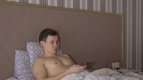 Man Lies in Bed Looking at Mobile Phone