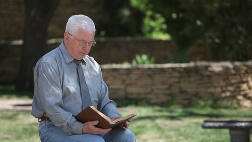Old Codger Granddad in Glasses Sits and Reads in a Street in Summer