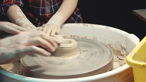 Child Learning Pottery with Adult Assistance on Wheel