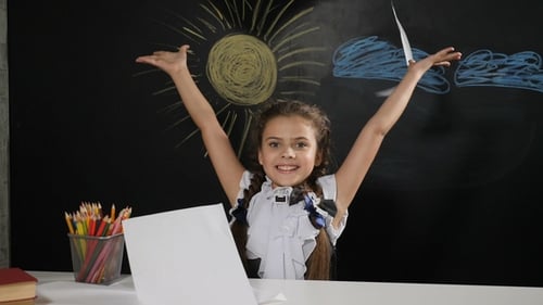 Jolie fille assise à un bureau avec un tableau noir derrière elle. Jetés d'écolière heureuse