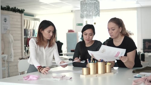 Eine Gruppe von Modedesignern diskutiert Skizzen von Kleidung und wählt einen Stoff für die Schneiderei