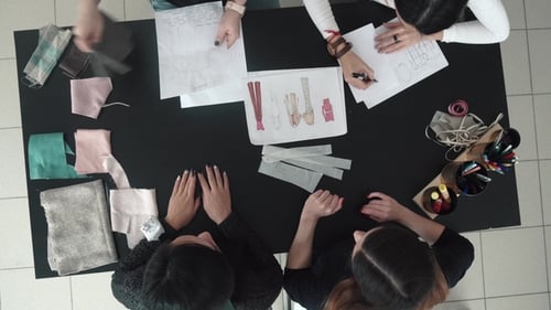 Group of Fashion Designers Discuss Sketches of Clothes and Choose a Fabric for Tailoring