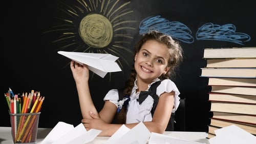 Concept de l'école. Jolie fille assise avec avion en papier à la main. Bureau et tableau derrière eux