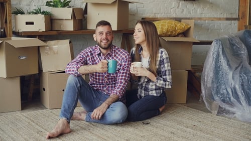 Happy Married Couple Clanging Mugs and Drinking Tea While Sitting on Floor in New Apartment After