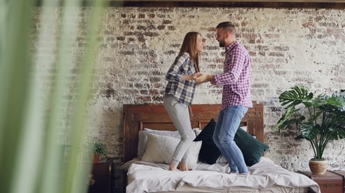 Happy Couple Jumping on Bed in Sunlit Room