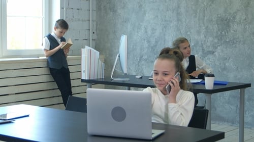 Portrait of a Little Girl Talking on the Phone and Working on Laptop in Office