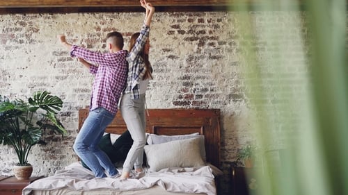 Young Couple Dances Together Back to Back on Bed