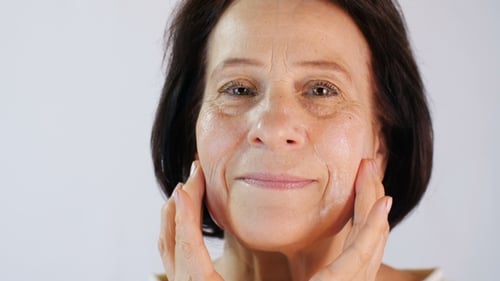 Woman Applies Moisturizer to Her Face in Close Up
