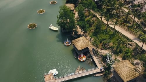 Exotic Bungalows with Thatched Roof and Boat Pier on Shore Green Lake Aerial View. Drone View