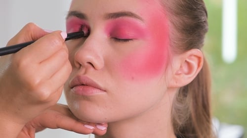 Maquillador profesional que aplica delineador de ojos alrededor de todo el ojo de la modelo en una habitación blanca
