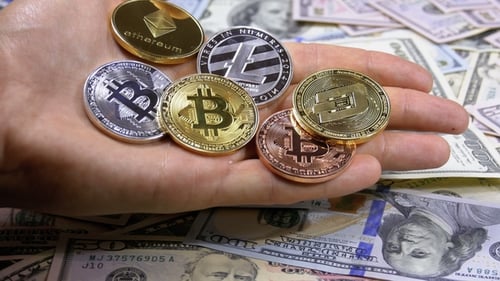La main tient différentes pièces de crypto-monnaie sur une table avec des dollars américains en rotation