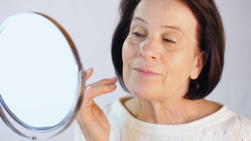 Senior Woman Applies Lotion to Her Face