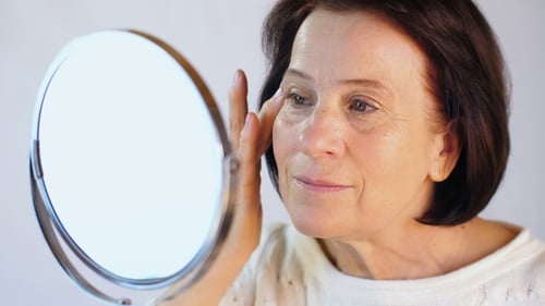 Elegant Woman Applying Lotion to Face in Mirror