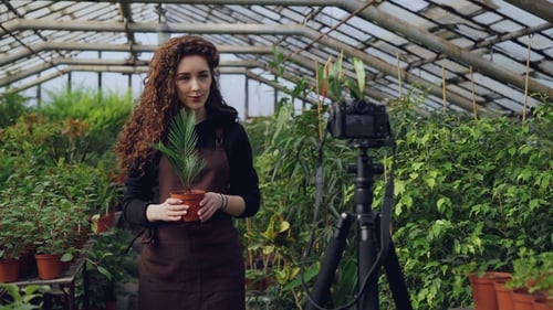 Woman Vlogging About Gardening in Greenhouse with Lush Plants