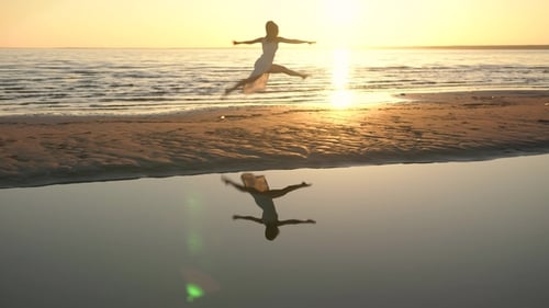 Junge Frau im weißen Kleid tanzt am Strand