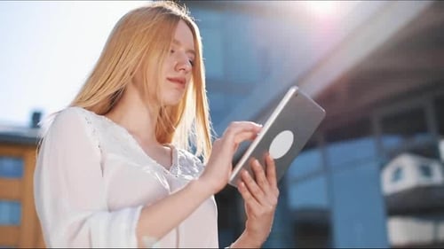 Pretty Young Blonde Woman Using Tablet Computer Device Outside on the Street. Woman Smiling, Tapping
