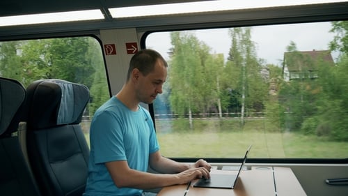 Mann arbeitet an seinem Laptop, während er mit dem Zug reist