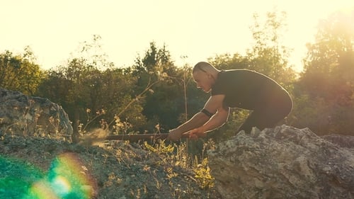 Der brutale Mann schlägt den Stein mit Hammer auf dem Felsen
