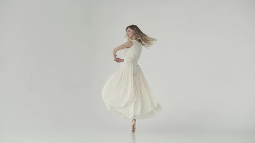 Ballerina in a Light Studio Dances in Pointe Shoes. Ballet Dancer in a Light Fluttering Long Dress