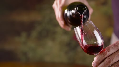 Männliche Hand gießt Rotwein in Glas aus der Flasche. Mann gießt Rotwein