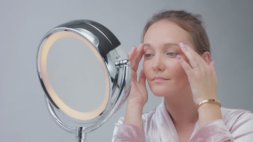 Woman Examines Face in Lighted Makeup Mirror